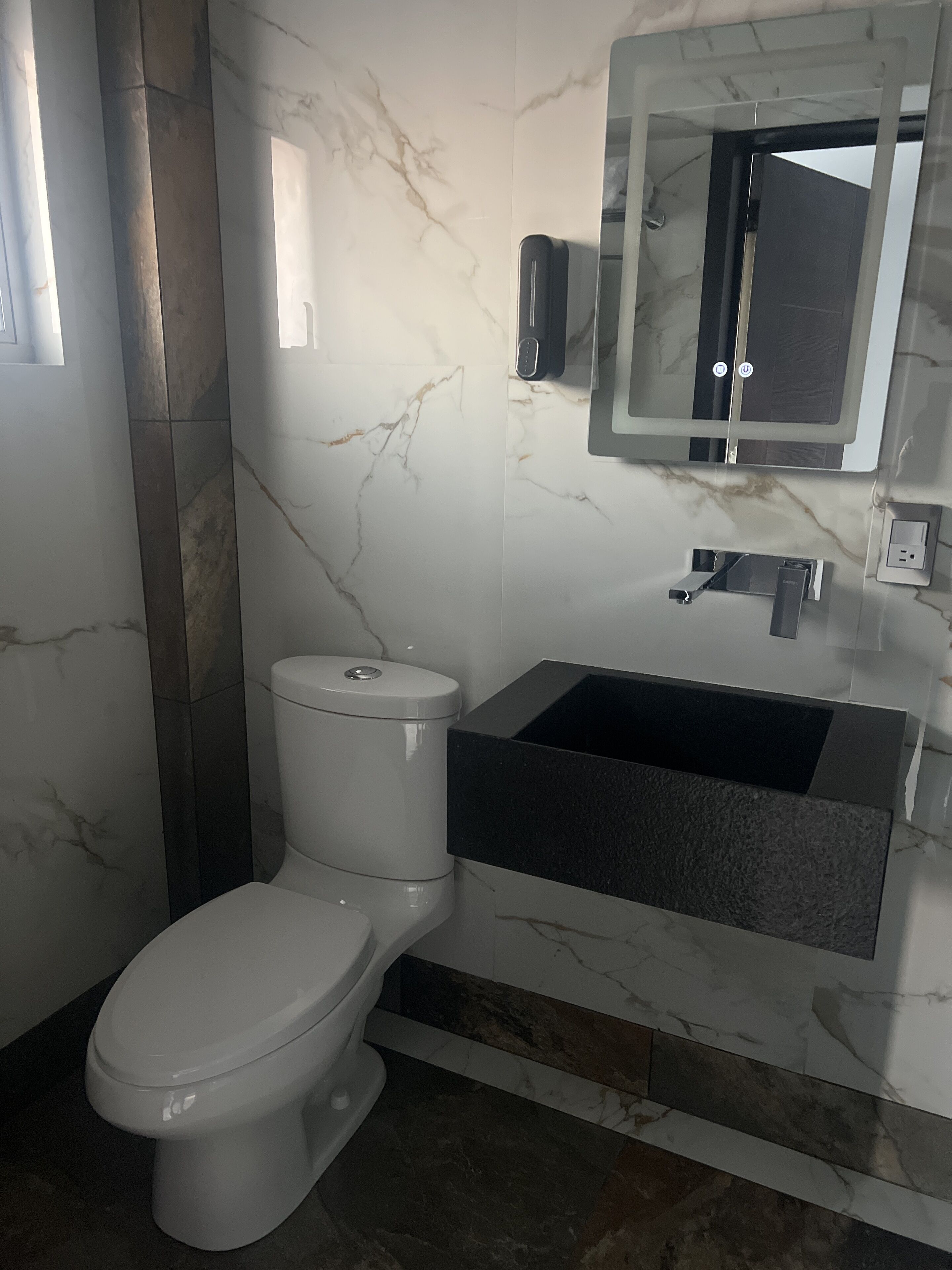 A modern bathroom with a toilet, a black sink, and a mirror.