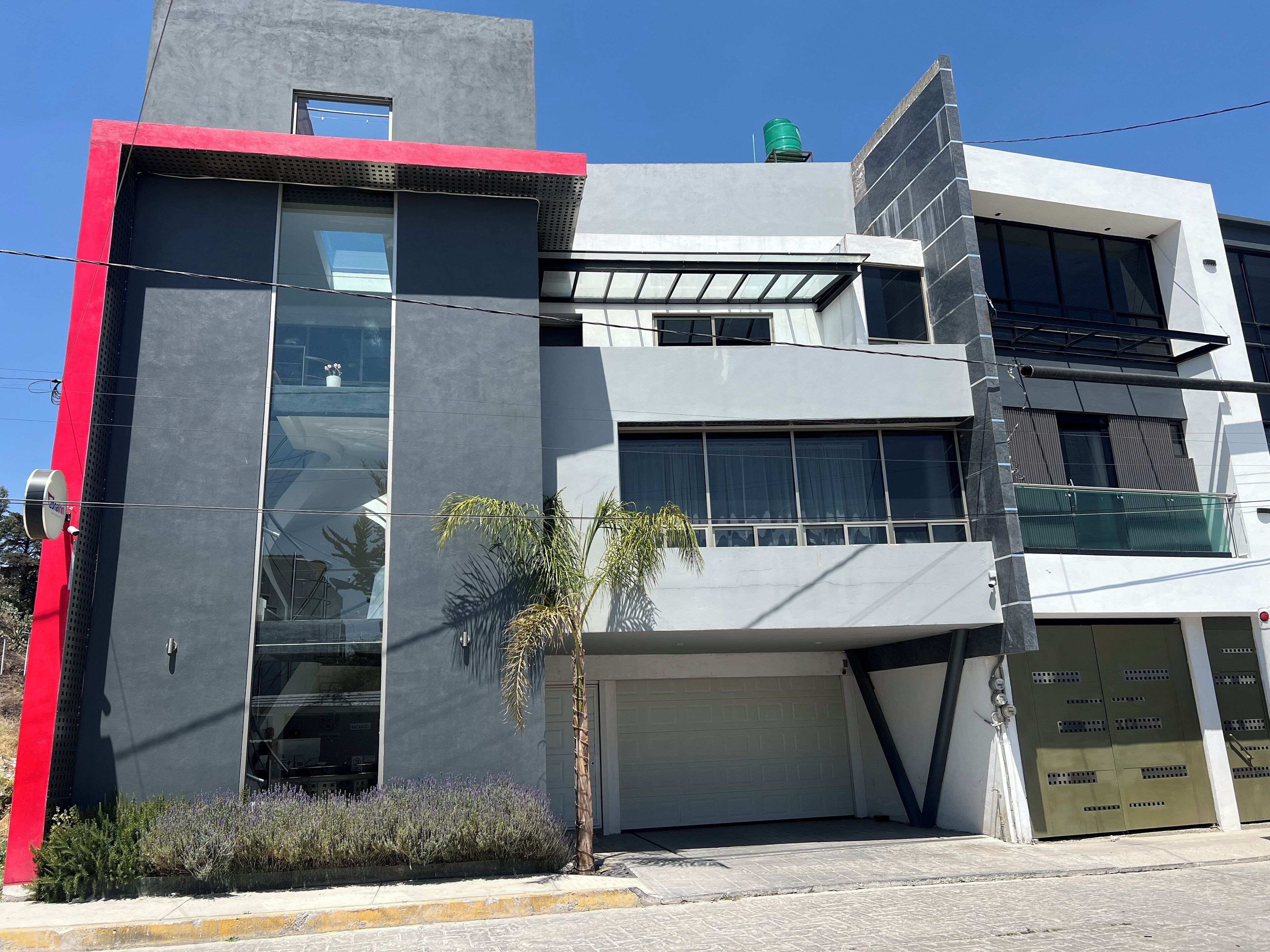 Un edificio moderno con garaje, ventanas amplias y una palmera pequeña.