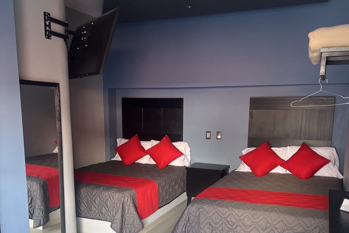 A hotel room with two beds, each with red and white bedding, a flat-screen TV mounted on the wall, and a mirror on the left side.