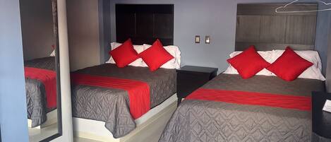 A hotel room with two beds, each with red and white bedding, a flat-screen TV mounted on the wall, and a mirror on the left side.