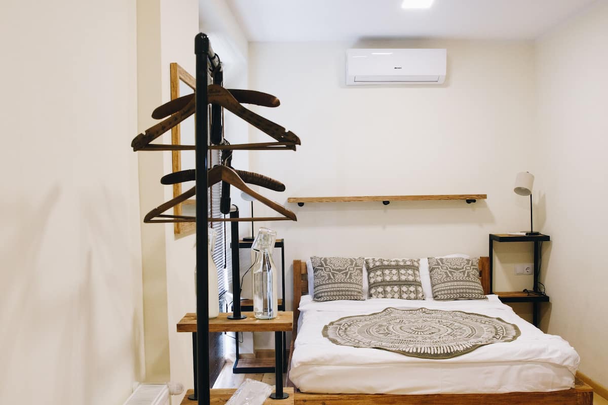 Un dormitorio con cama de madera, perchero de madera, mesita de noche con lámpara y radiador.