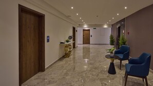 A hotel lobby with a marble floor, wooden doors, a reception desk, and blue chairs. - Grand Continent Hebbal a Sarovar Portico Affiliate Hotel (Bengaluru)
