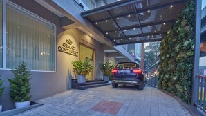 A hotel entrance with a canopy, potted plants, and a car parked outside. - Grand Continent Hebbal a Sarovar Portico Affiliate Hotel (Bengaluru)