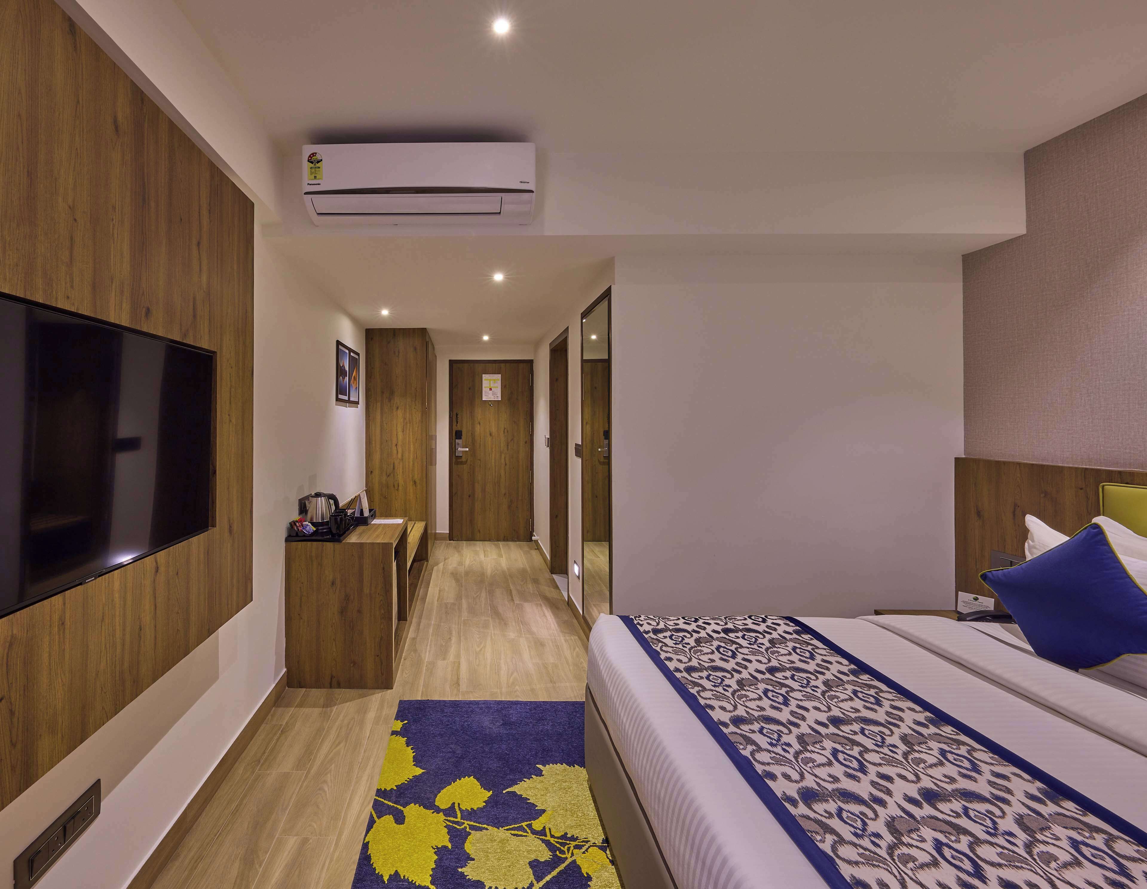Une chambre d’hôtel équipée d’une télévision à écran plat, d’un lit avec une literie à motifs, d’un bureau avec une chaise et d’un appareil de climatisation.