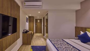 Une chambre d’hôtel équipée d’une télévision à écran plat, d’un lit avec une literie à motifs, d’un bureau avec une chaise et d’un appareil de climatisation.