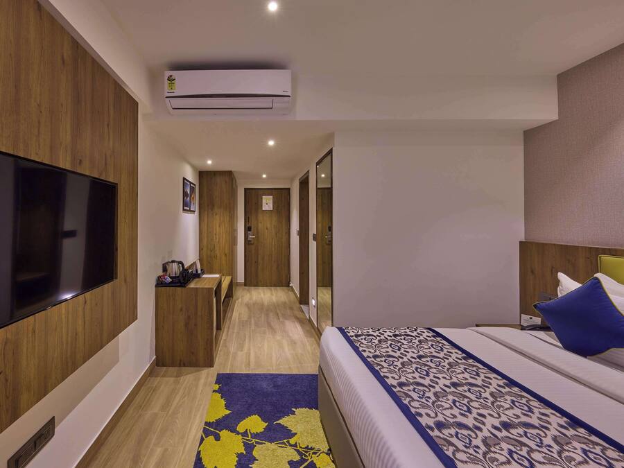 Une chambre d’hôtel équipée d’une télévision à écran plat, d’un lit avec une literie à motifs, d’un bureau avec une chaise et d’un appareil de climatisation.