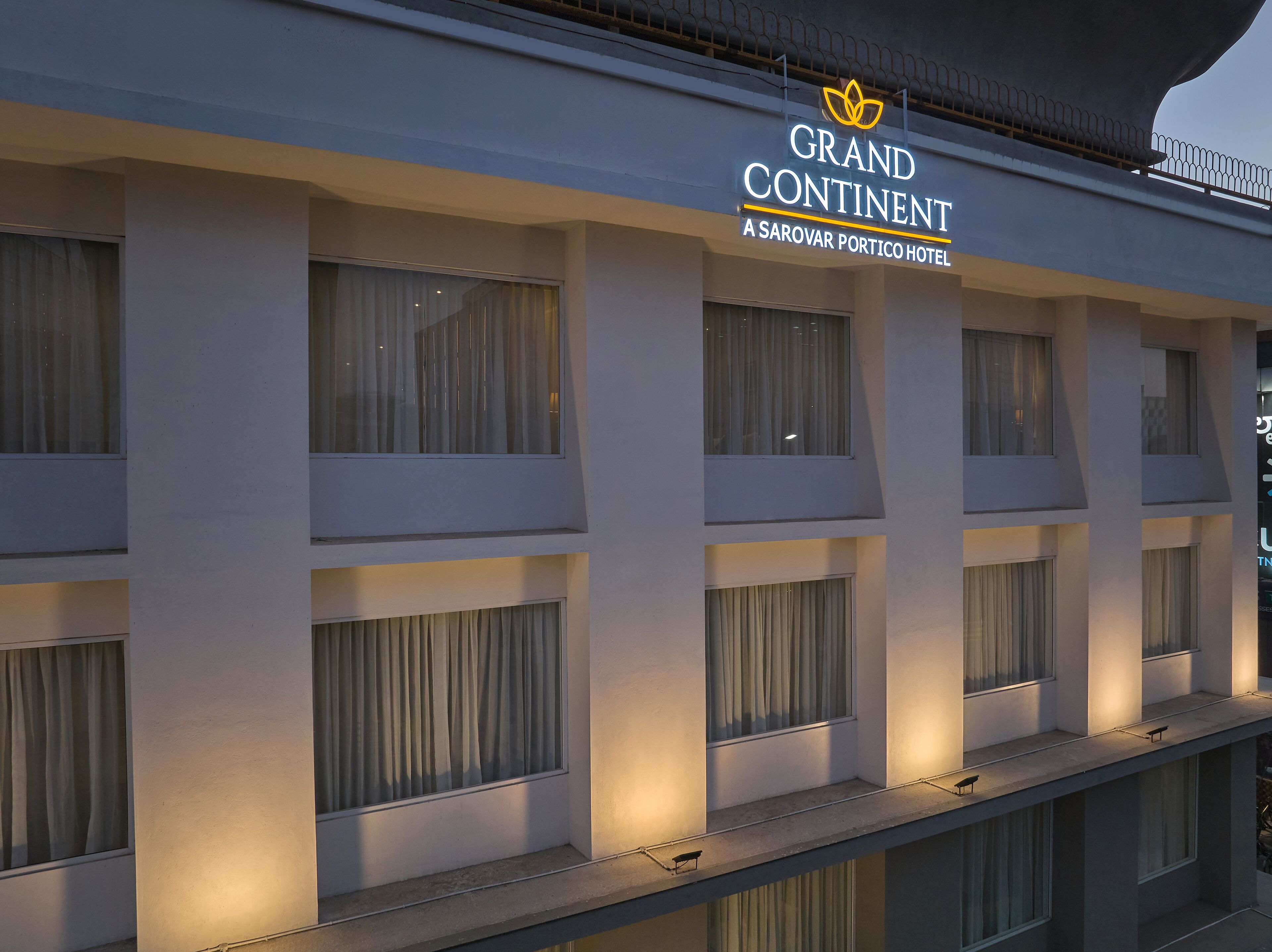 La façade d’un hôtel, ornée de nombreuses fenêtres, et une enseigne indiquant : « Grand Continental, un hôtel du groupe Sarovar Portico ».