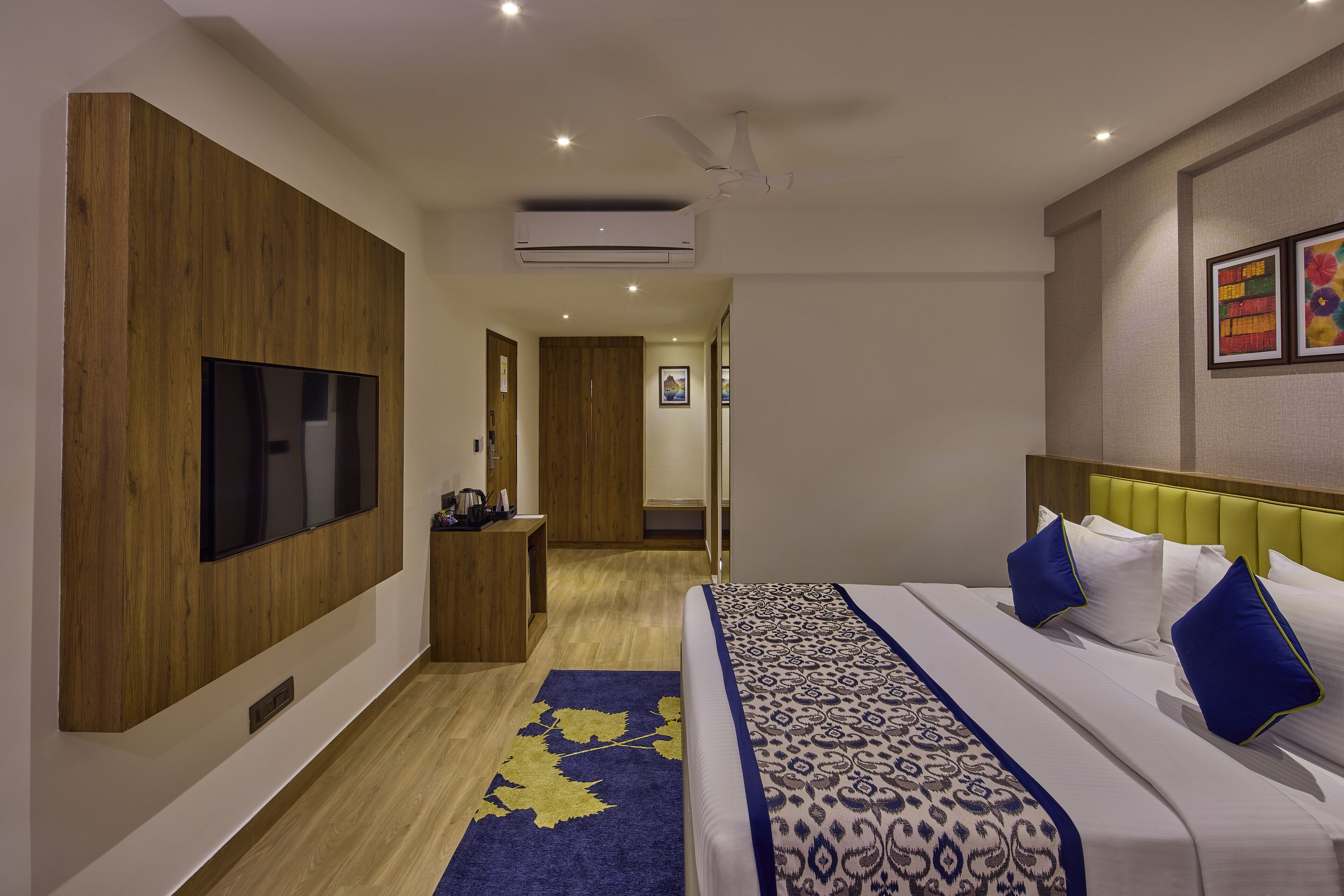 Habitación de hotel con una cama grande, un televisor de pantalla plana montado en la pared, un diseño de paneles de madera en una pared y un ventilador de techo.