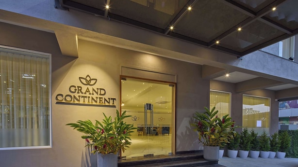 The exterior of a hotel named "Grand Continent" with a glass entrance, potted plants, and a modern architectural design. - Grand Continent Hebbal a Sarovar Portico Affiliate Hotel (Bengaluru)