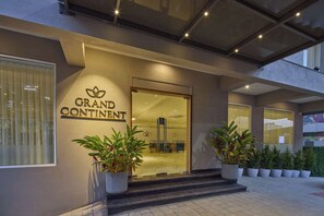 The exterior of a hotel named "Grand Continent" with a glass entrance, potted plants, and a modern architectural design. - Grand Continent Hebbal a Sarovar Portico Affiliate Hotel (Bengaluru)