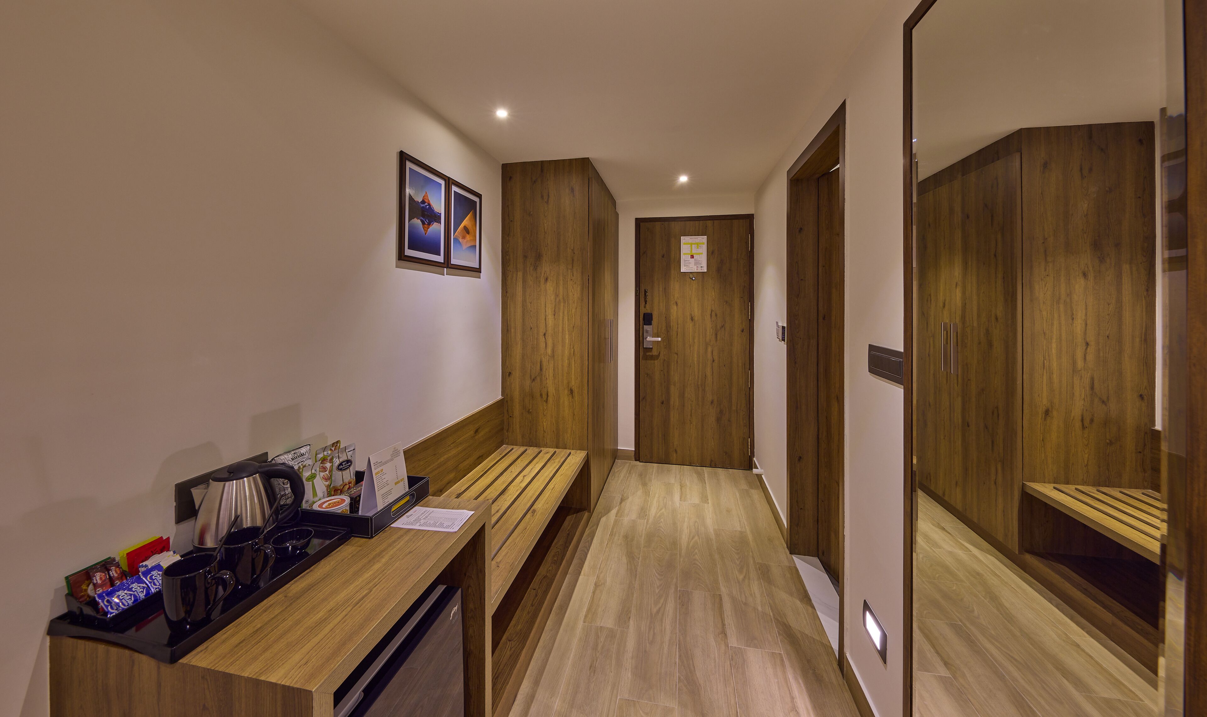A hotel hallway with wooden flooring, a reception desk with a coffee machine, and a mirror on the right.