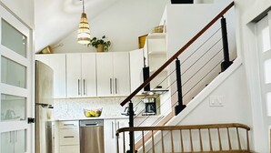 A modern kitchen with white cabinets, a wooden staircase, and a hanging light fixture. - NEW:  Oceanfront, Newly Remodeled 2 bedroom condo,  WiFi, AC  (Princeville)