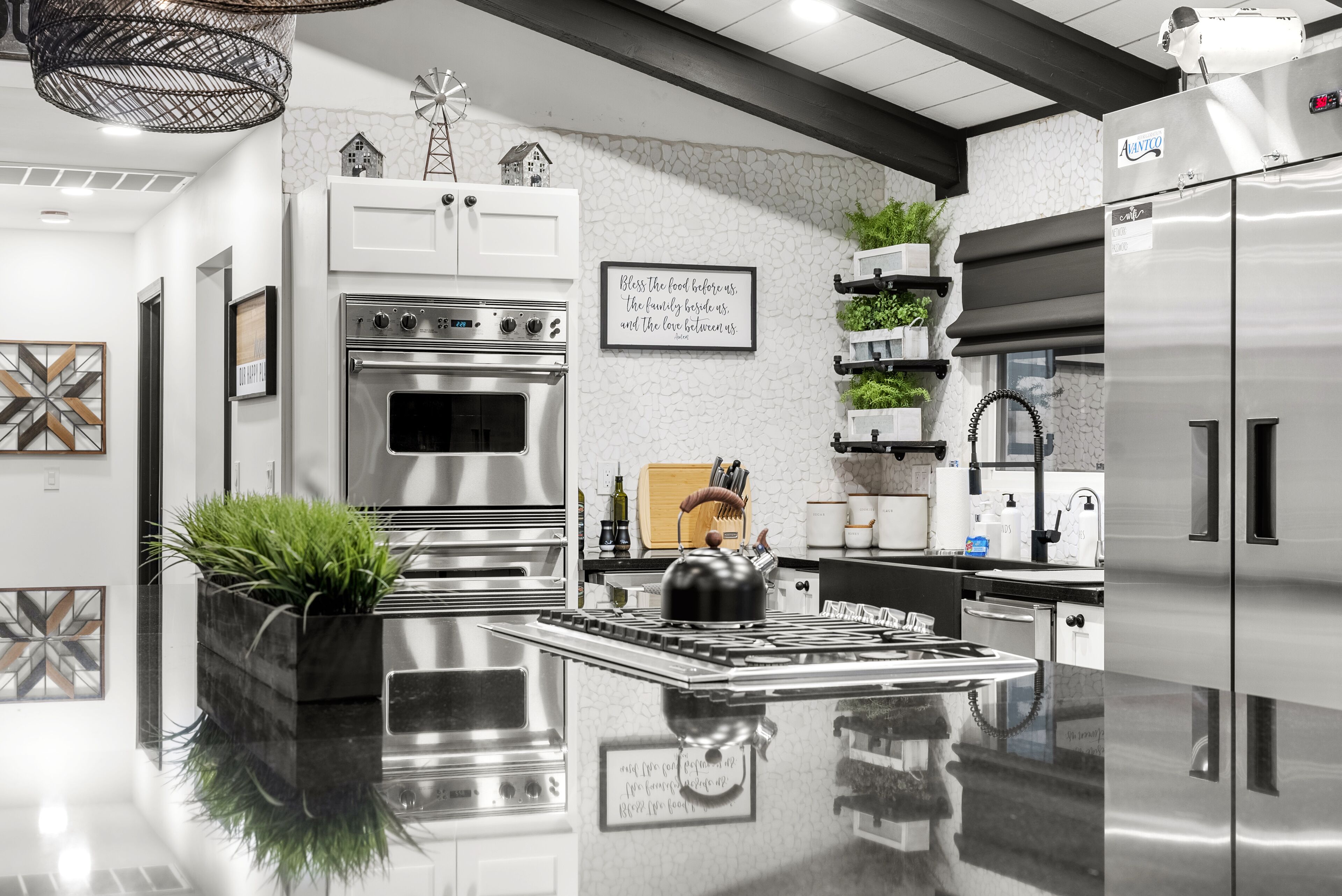 A modern kitchen with a central island, stainless steel appliances, and decorative elements like a windmill and a framed quote on the wall.