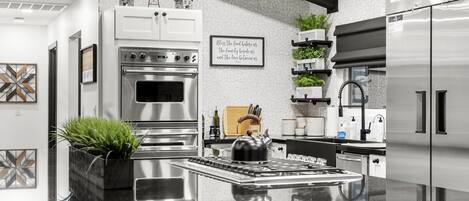 A modern kitchen with a central island, stainless steel appliances, and decorative elements like a windmill and a framed quote on the wall.