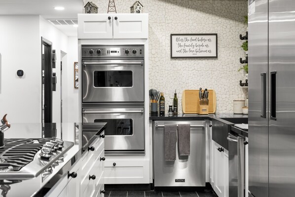 A modern kitchen with stainless steel appliances, white cabinetry, and a decorative wall sign.