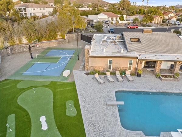 A residential property with a swimming pool, a tennis court, and a patio area with lounge chairs.