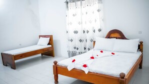 A room with two wooden beds, white bedding, and a patterned curtain.