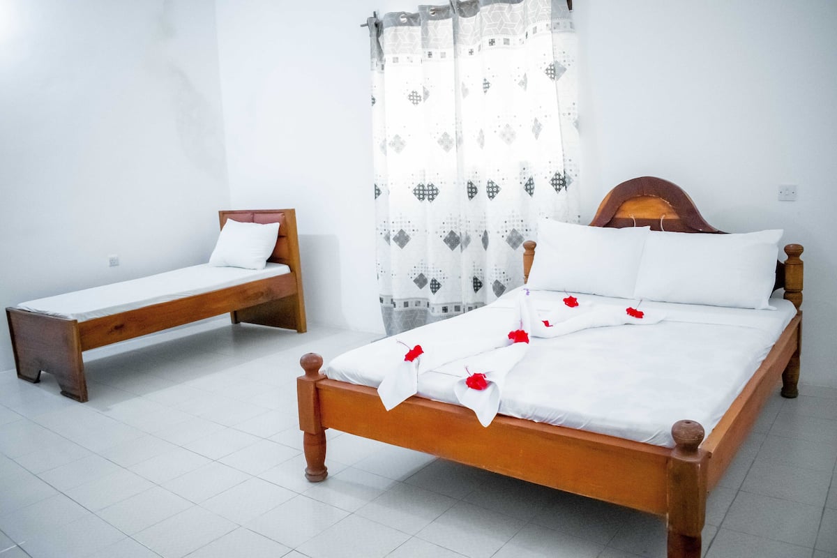 A room with two wooden beds, white bedding, and a patterned curtain.