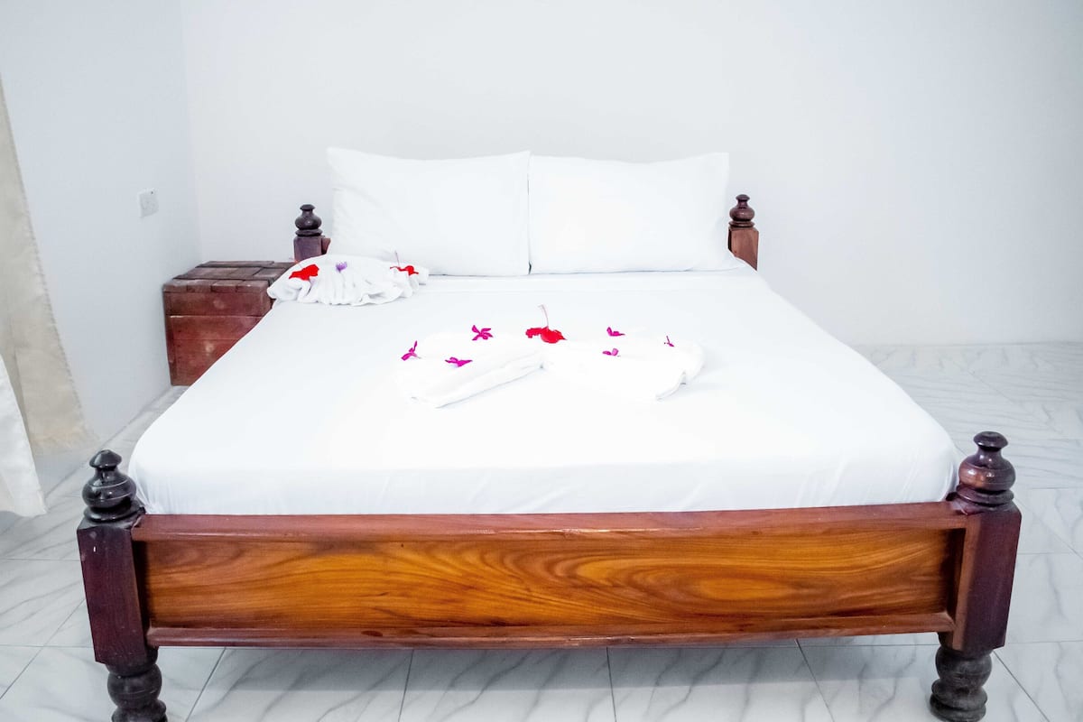 A neatly made bed with white linens, a wooden headboard, and a small wooden nightstand beside it.