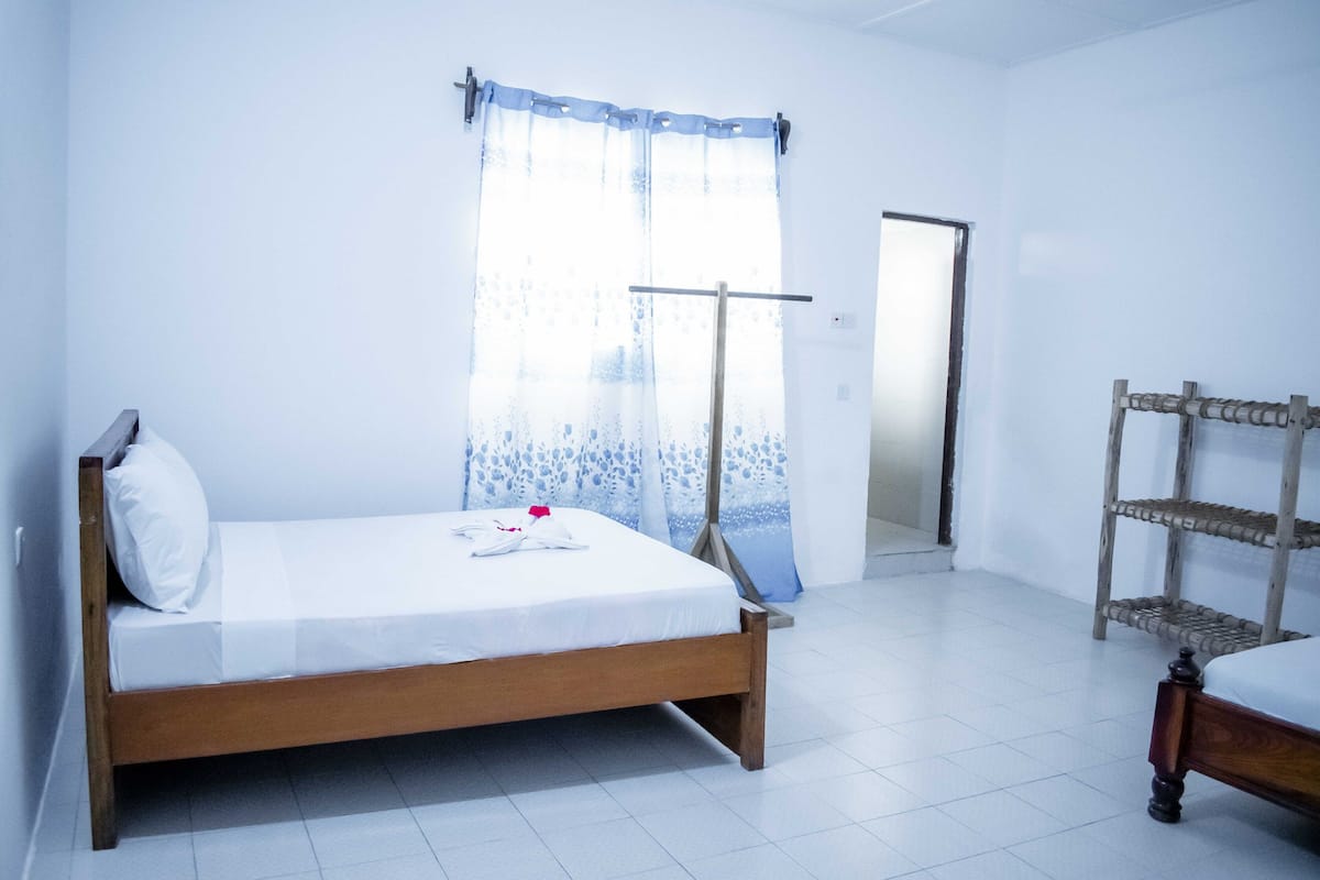 A bedroom with a wooden bed, a window with a sheer curtain, and a wooden shelf unit.