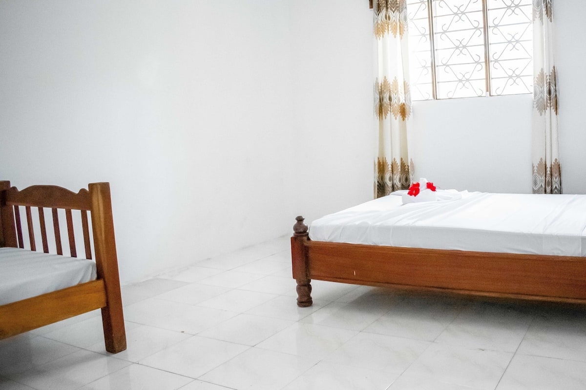 A single bed with a wooden frame and white bedding in a room with white walls and a tiled floor.