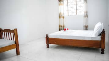 Uma cama de solteiro com estrutura de madeira e roupa de cama branca num quarto com paredes brancas e chão de azulejos.