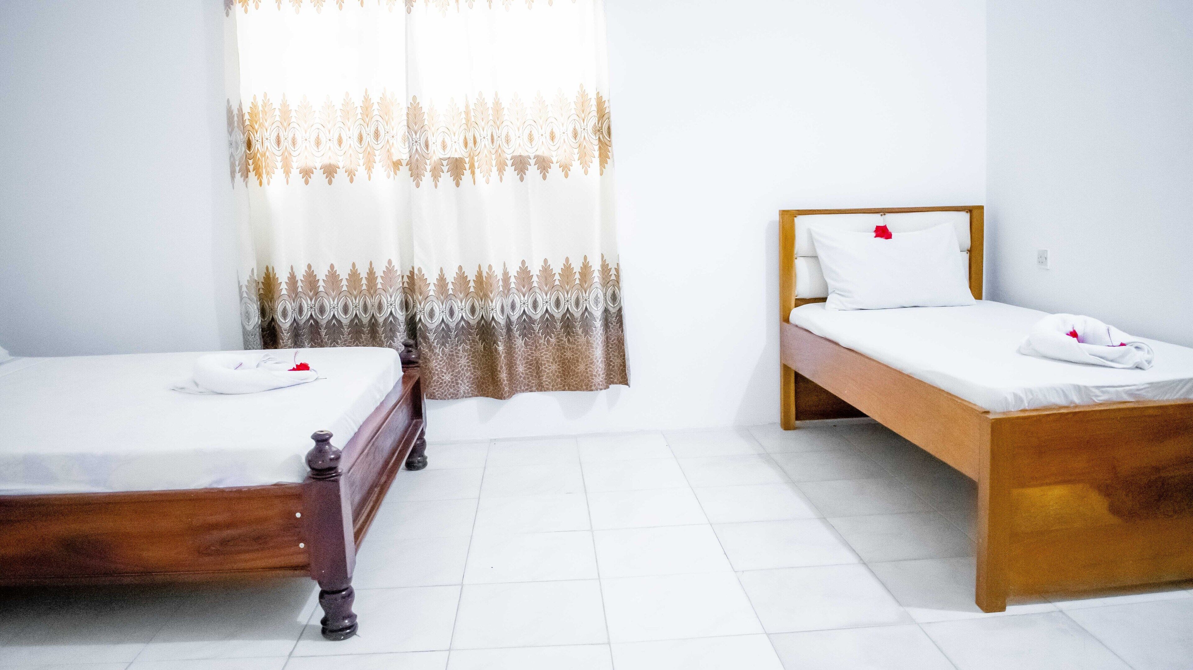 Una habitación con dos camas de madera, ropa de cama blanca y una ventana con cortinas estampadas.