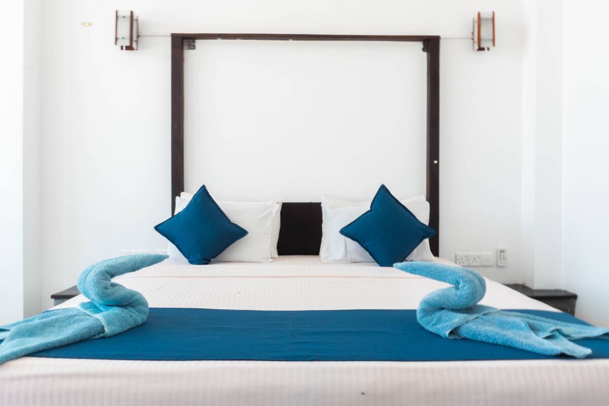 A bed with a headboard, pillows, and a blue blanket.