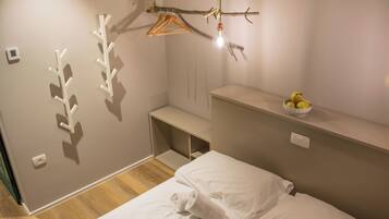 A bedroom with a bed, a small shelf with fruit, a coat rack, and a wall-mounted light fixture.