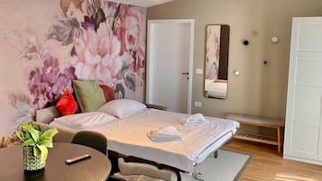 A hotel room with a bed, a round table with chairs, a large floral wall mural, a mirror, and a wardrobe.