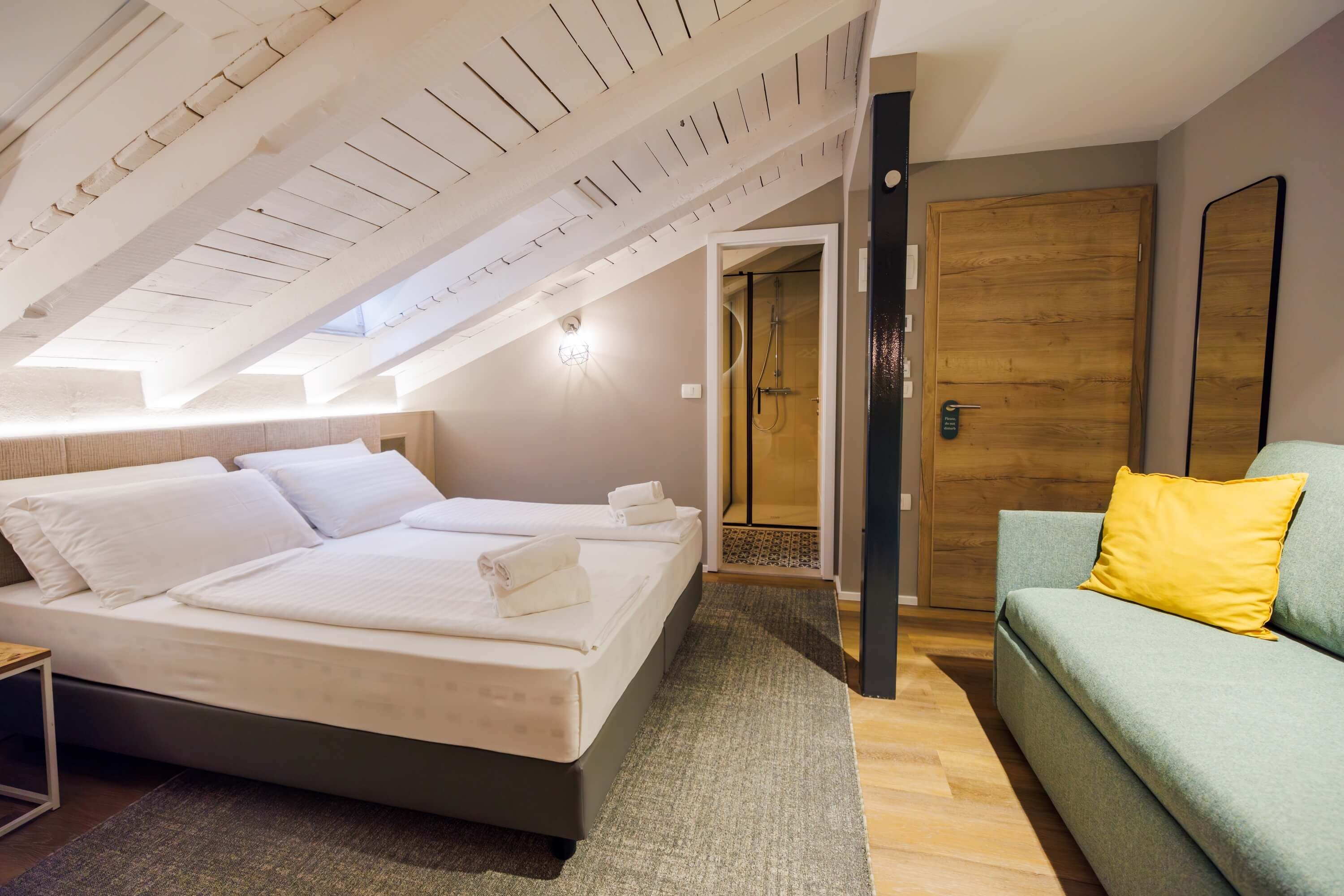 A bedroom with a bed, a wooden door, a green sofa, and a shower area.