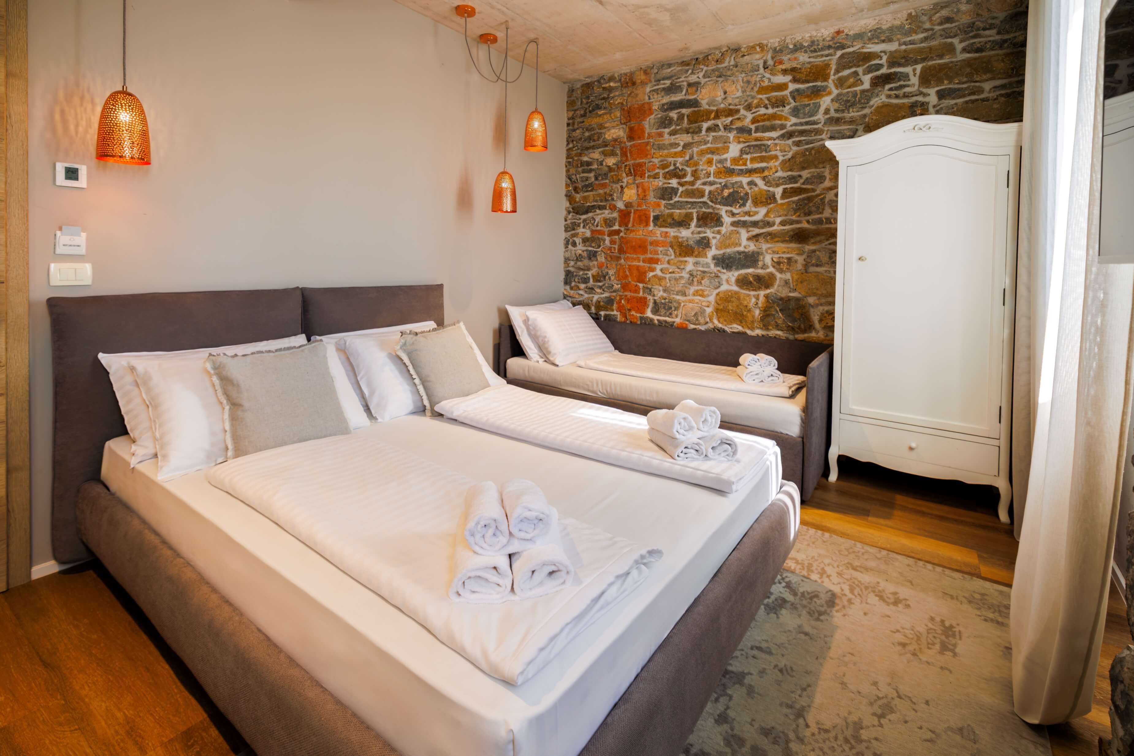 Een hotelkamer met een groot bed, een kleiner bed, een kledingkast en een stenen muur.