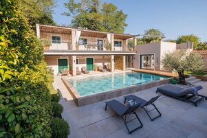 Una piscina al aire libre, sombrillas, sillones reclinables de piscina