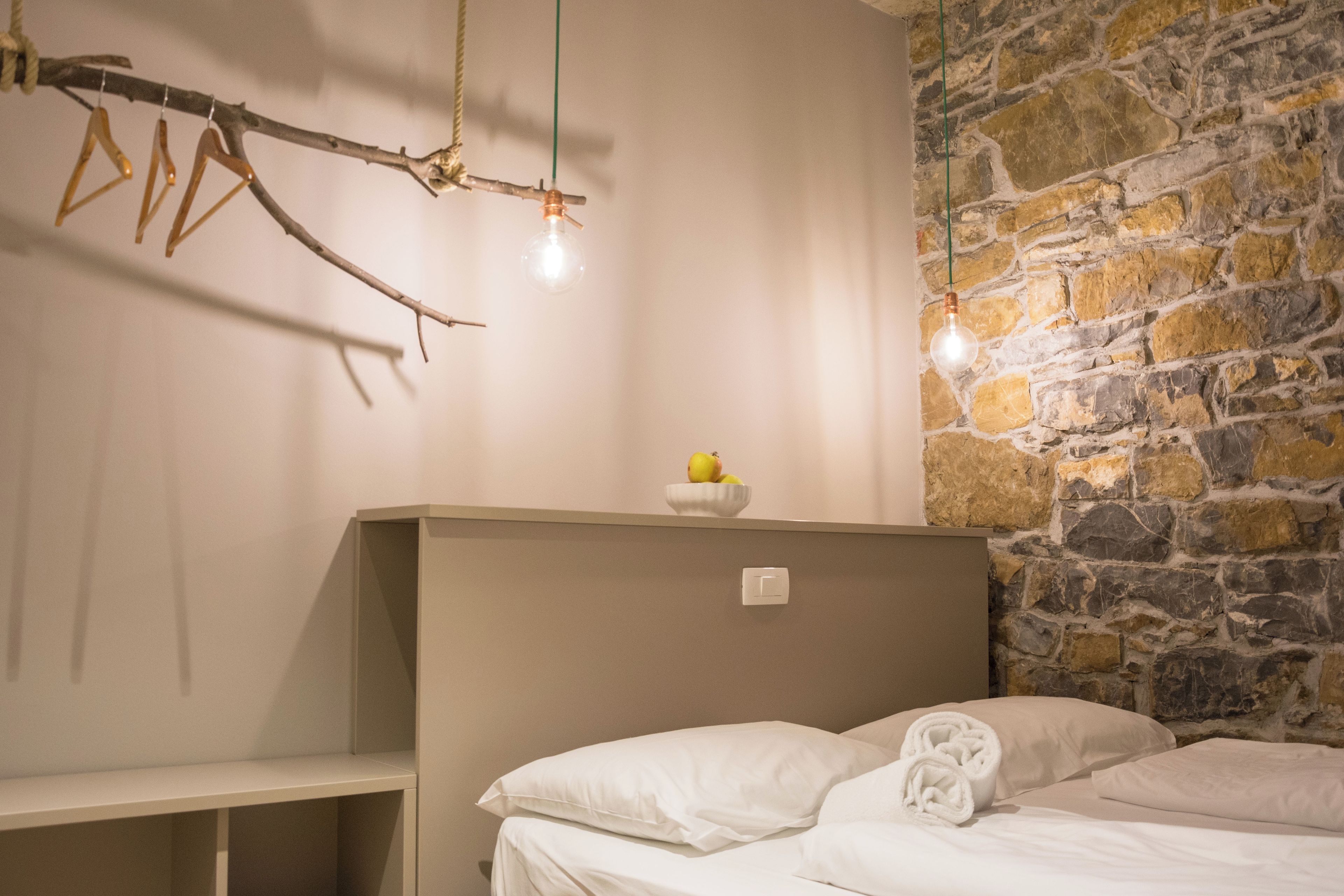 A bedroom with a stone wall, a bed with white linens, a bedside table, and a hanging light fixture.