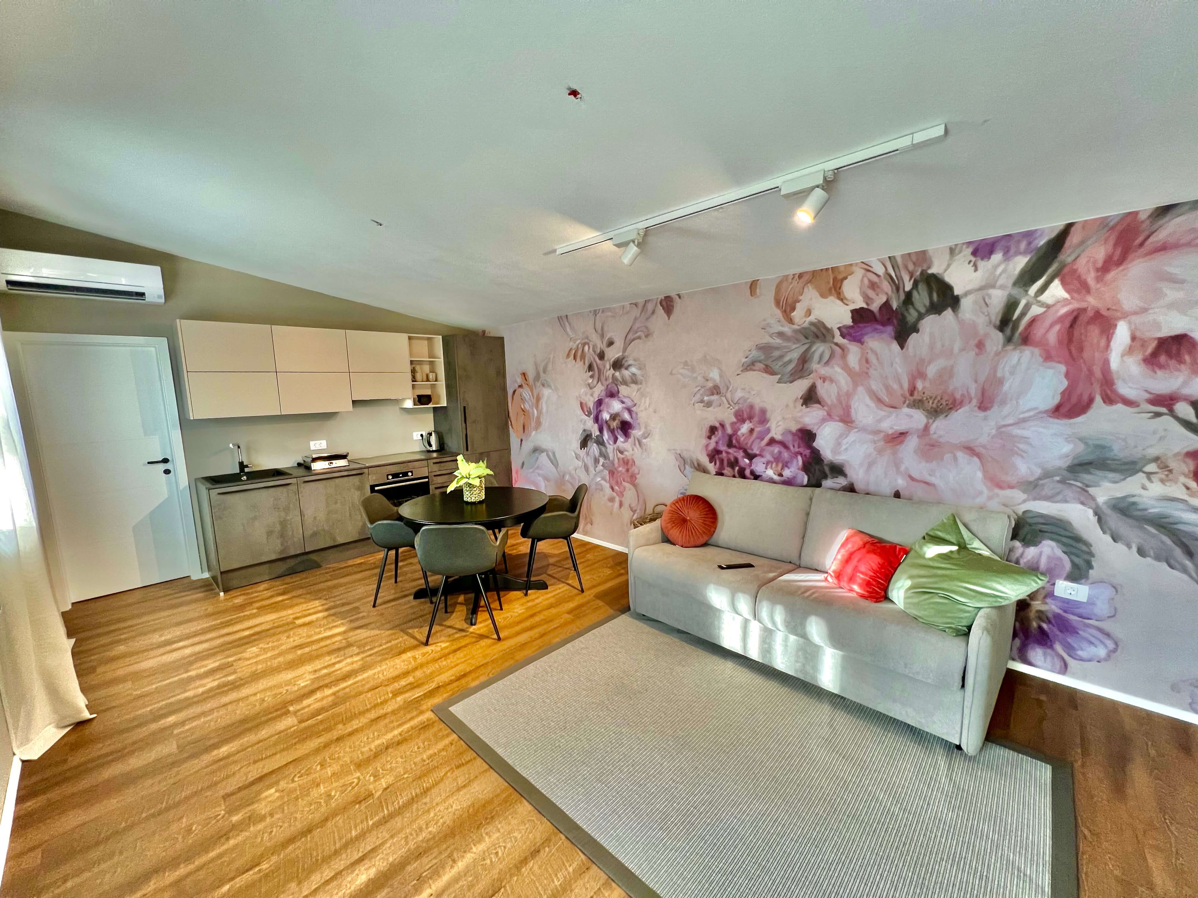 A modern living space with a kitchen, dining area, and a sofa with a floral wall mural.