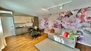 A modern living space with a kitchen, dining area, and a sofa with a floral wall mural.