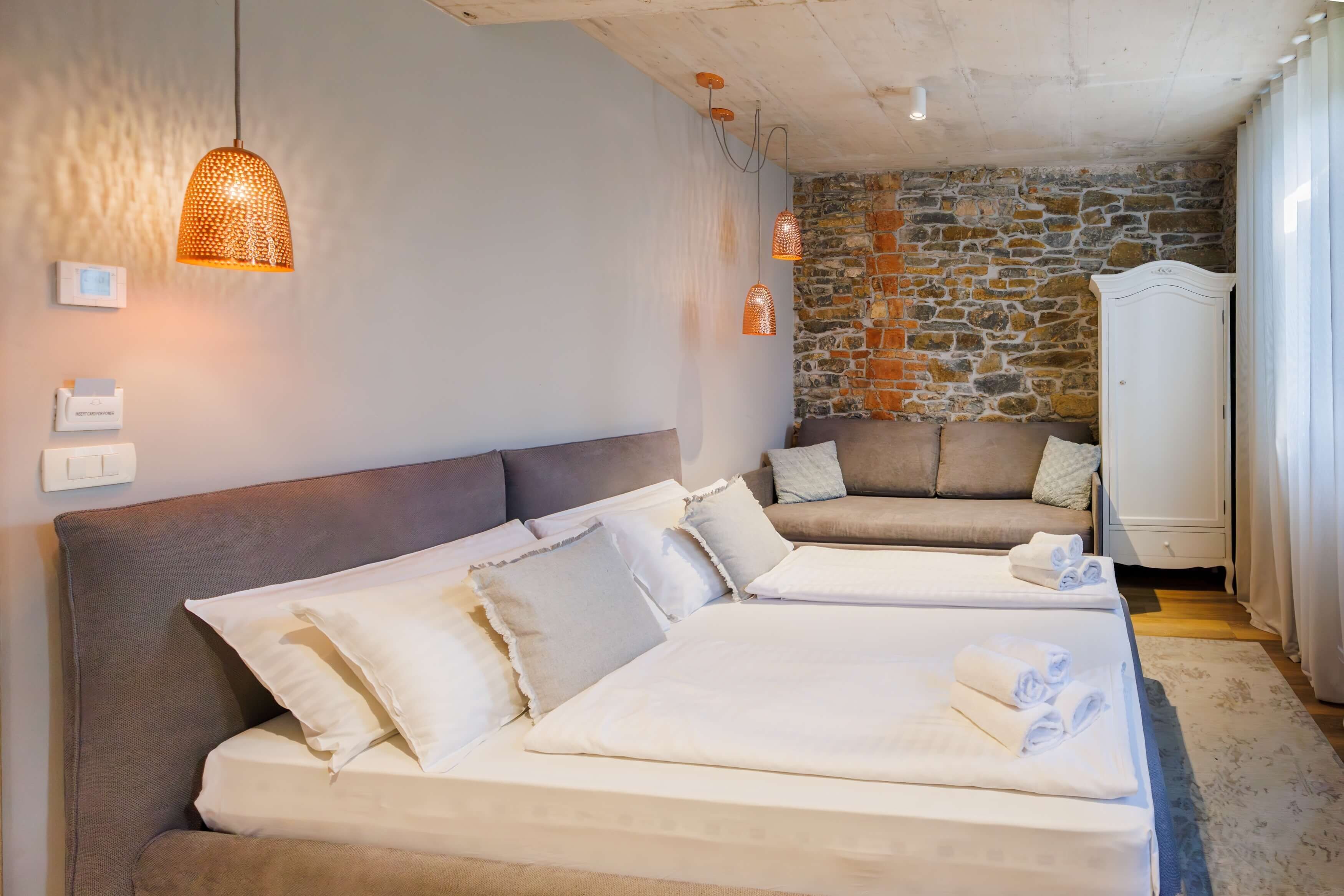 Habitación de hotel con pared de piedra, dos camas, un sofá y un armario.