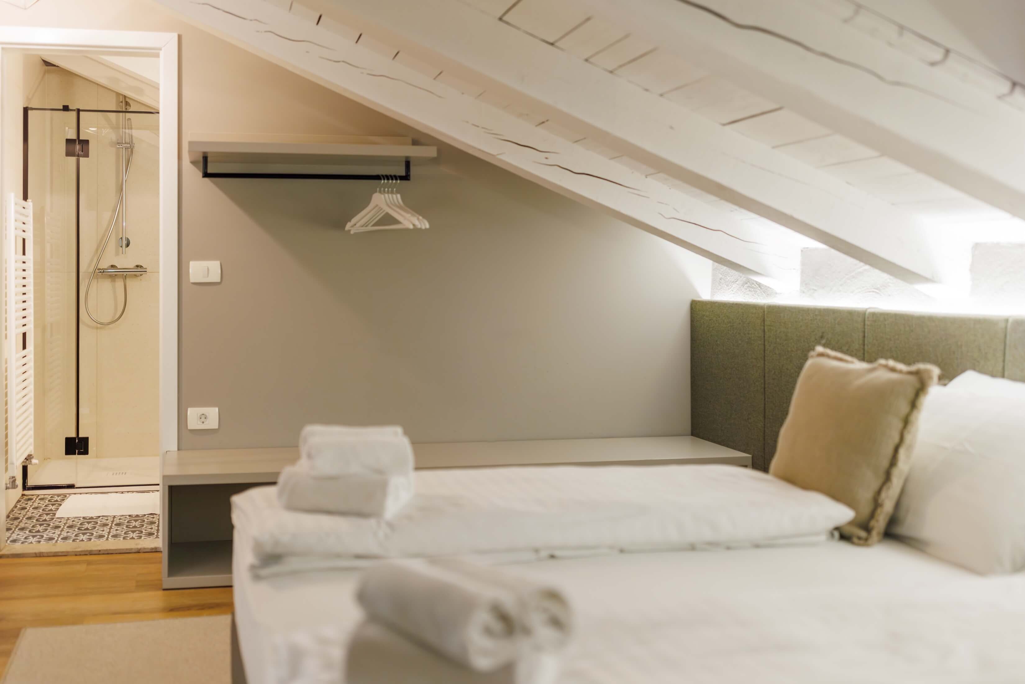 Ein modernes Schlafzimmer mit Schräge, einem Bett mit weißer Bettwäsche, einem Nachttisch und einer hängenden Leuchte.