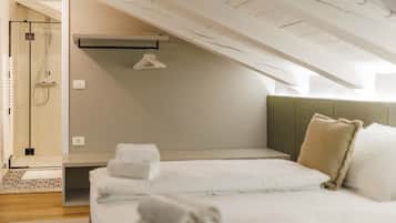 Un dormitorio moderno con techo inclinado, una cama con ropa de cama blanca, una mesita de noche y una lámpara colgante.