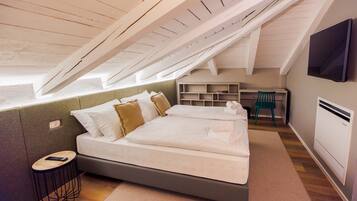 Une chambre avec un plafond de style industriel, un lit avec de nombreux oreillers, un bureau avec une chaise et un téléviseur fixé au mur.