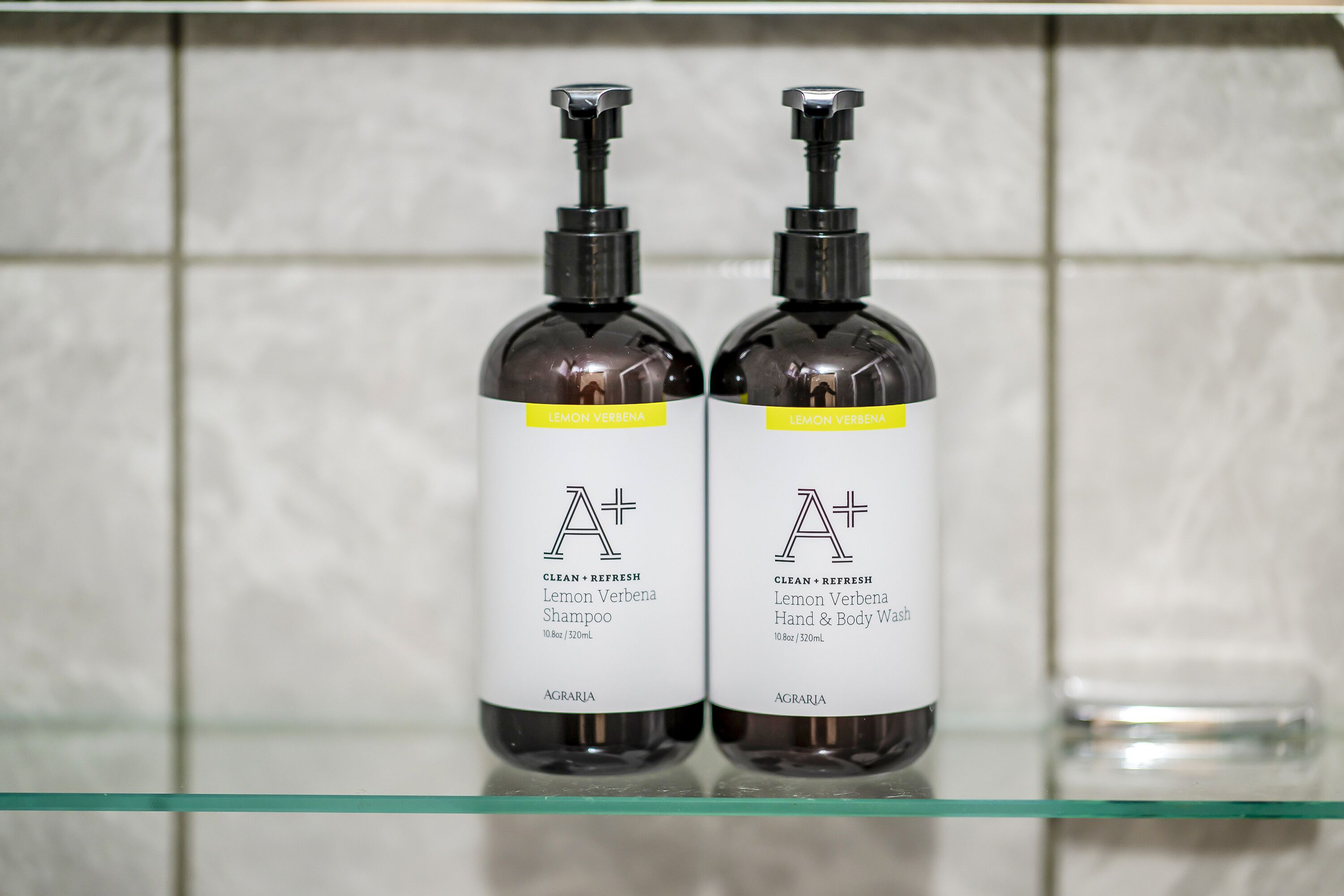 Two bottles of Lemon Verbena shampoo and hand & body wash on a glass shelf.