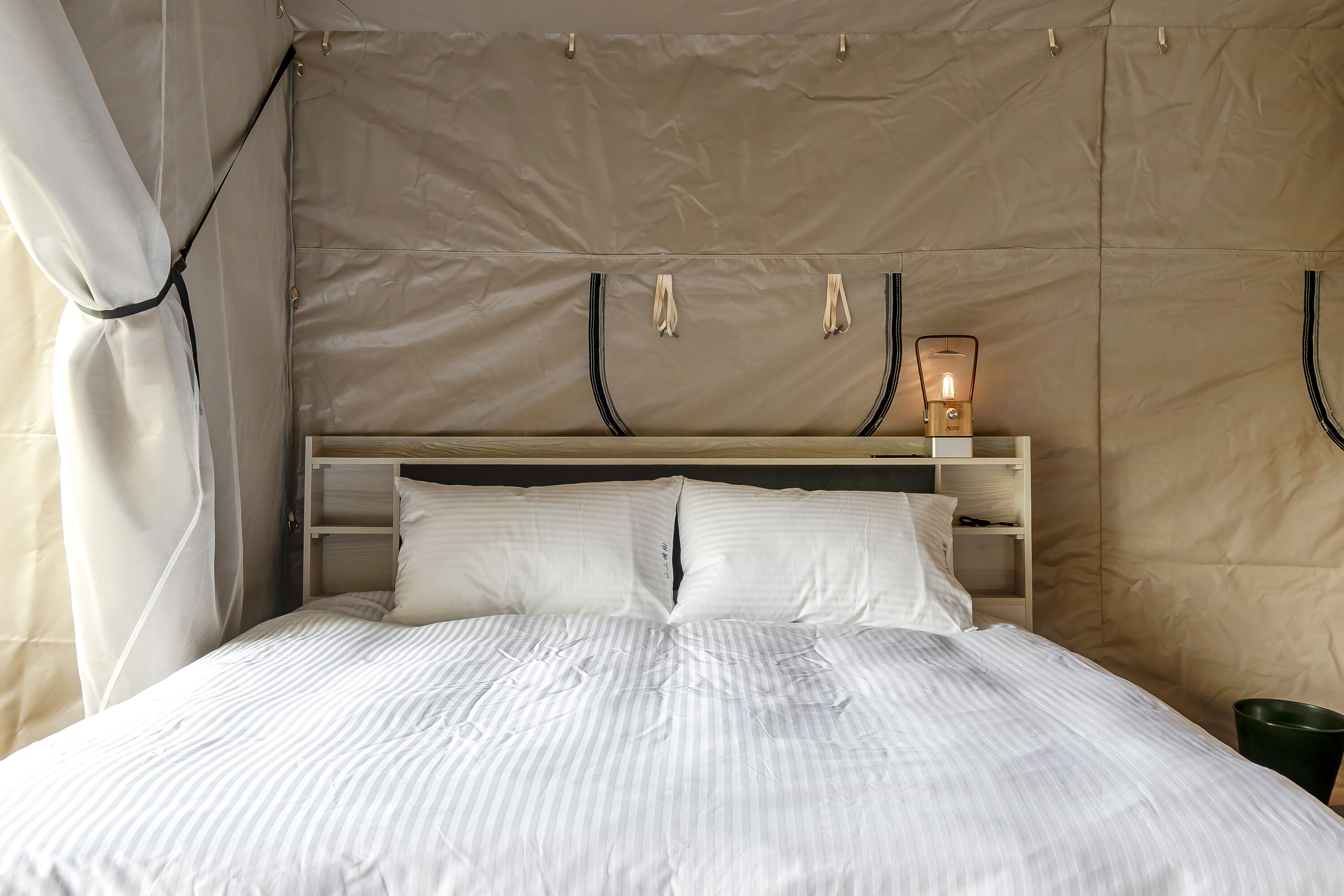 A bed with white striped bedding, a wooden headboard, and a bedside lamp.
