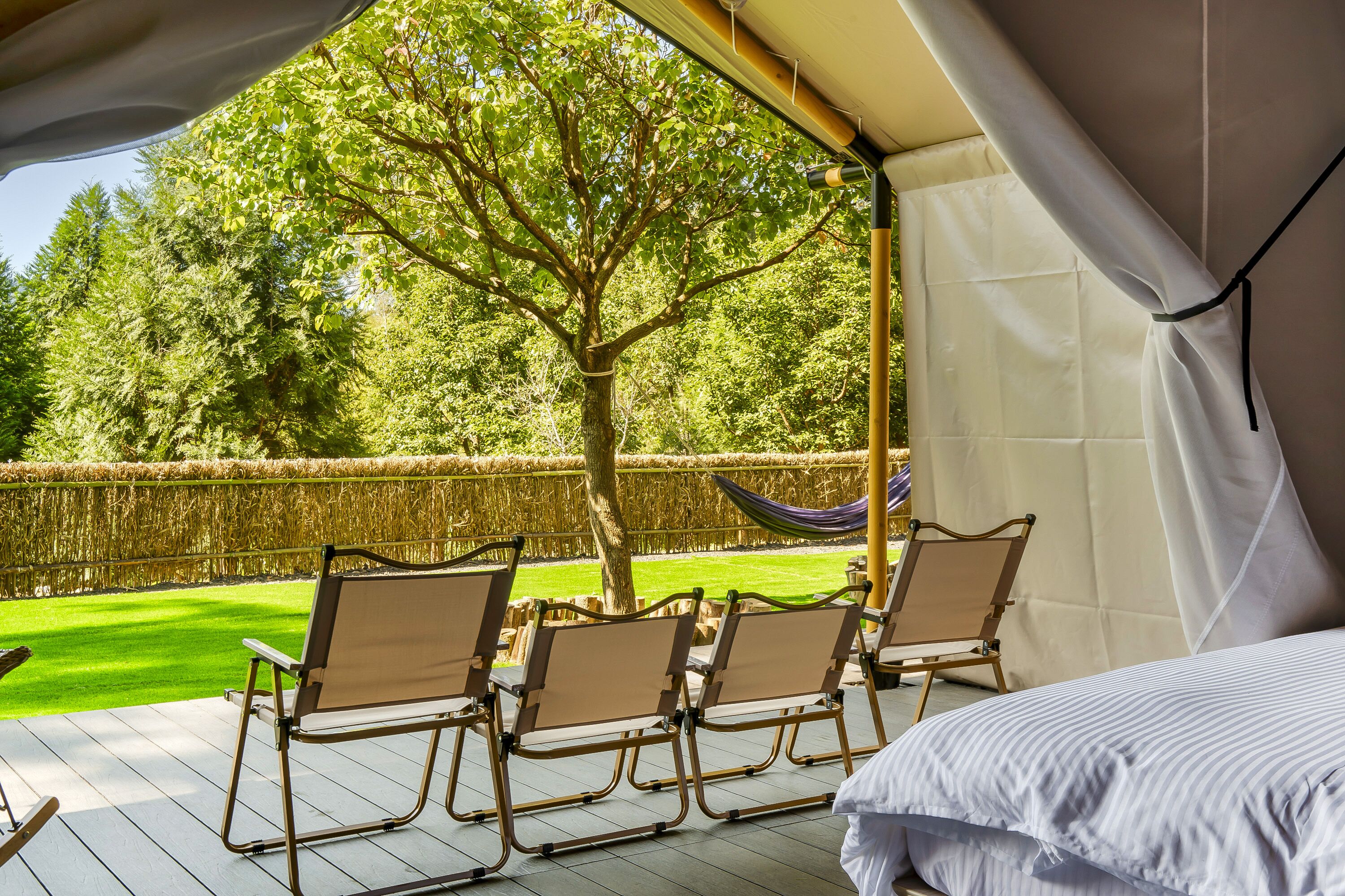 Een overdekt terras met stoelen en een hangmat, met uitzicht op een verzorgd gazon en bomen.