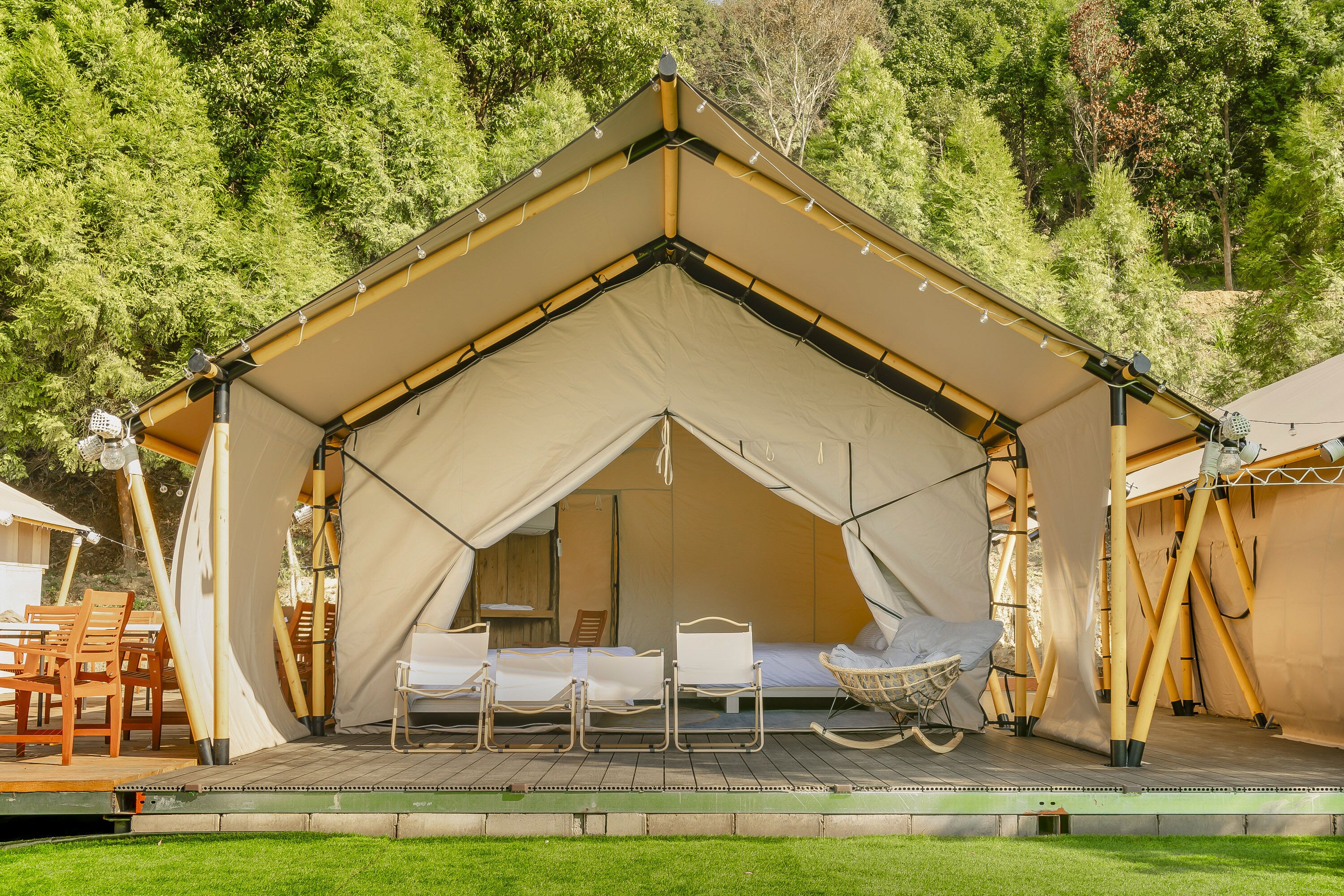 A tented accommodation with a wooden deck, two white beds, and a hanging chair.