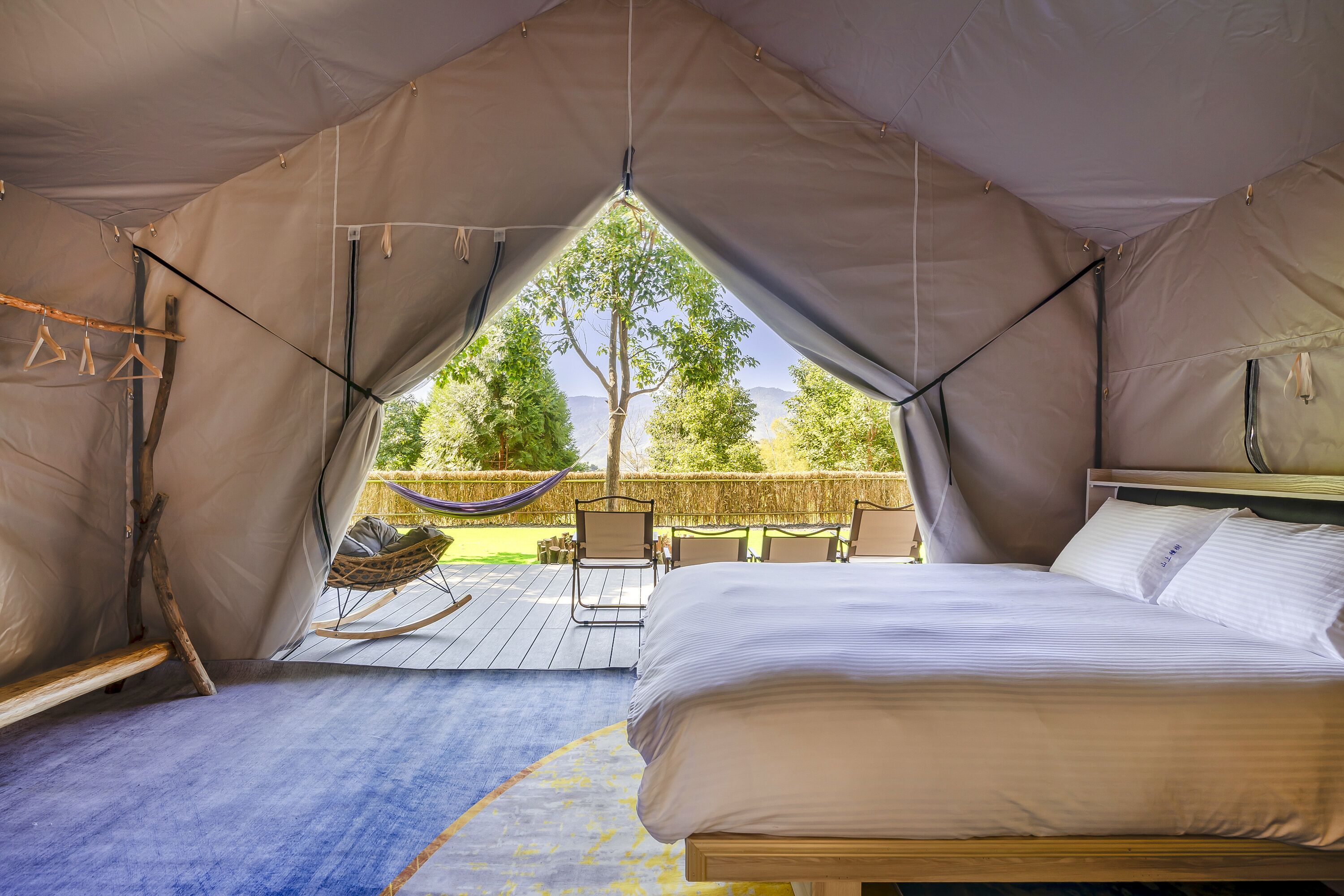 Alojamiento con tienda de campaña, cama, hamaca y vistas a árboles y montañas.