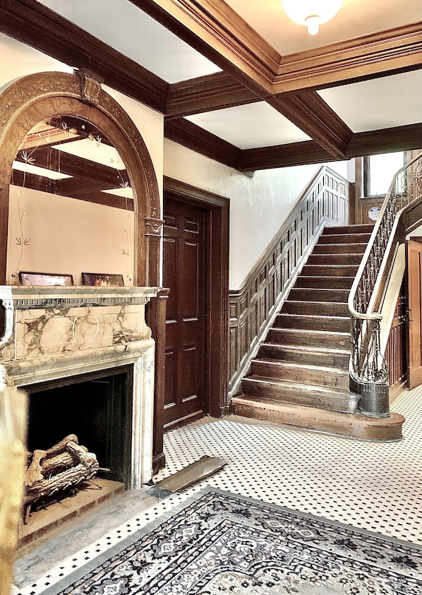 A grand staircase with a wooden handrail and a patterned carpet leading to a landing. - The Dery House  (Catasauqua)