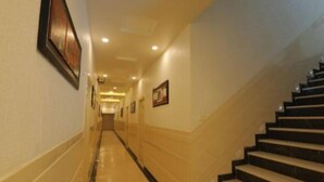 A hotel hallway with a marble floor, a staircase on the right, and framed pictures on the walls. - Hotel Sahibs Red Carpet (Agra)