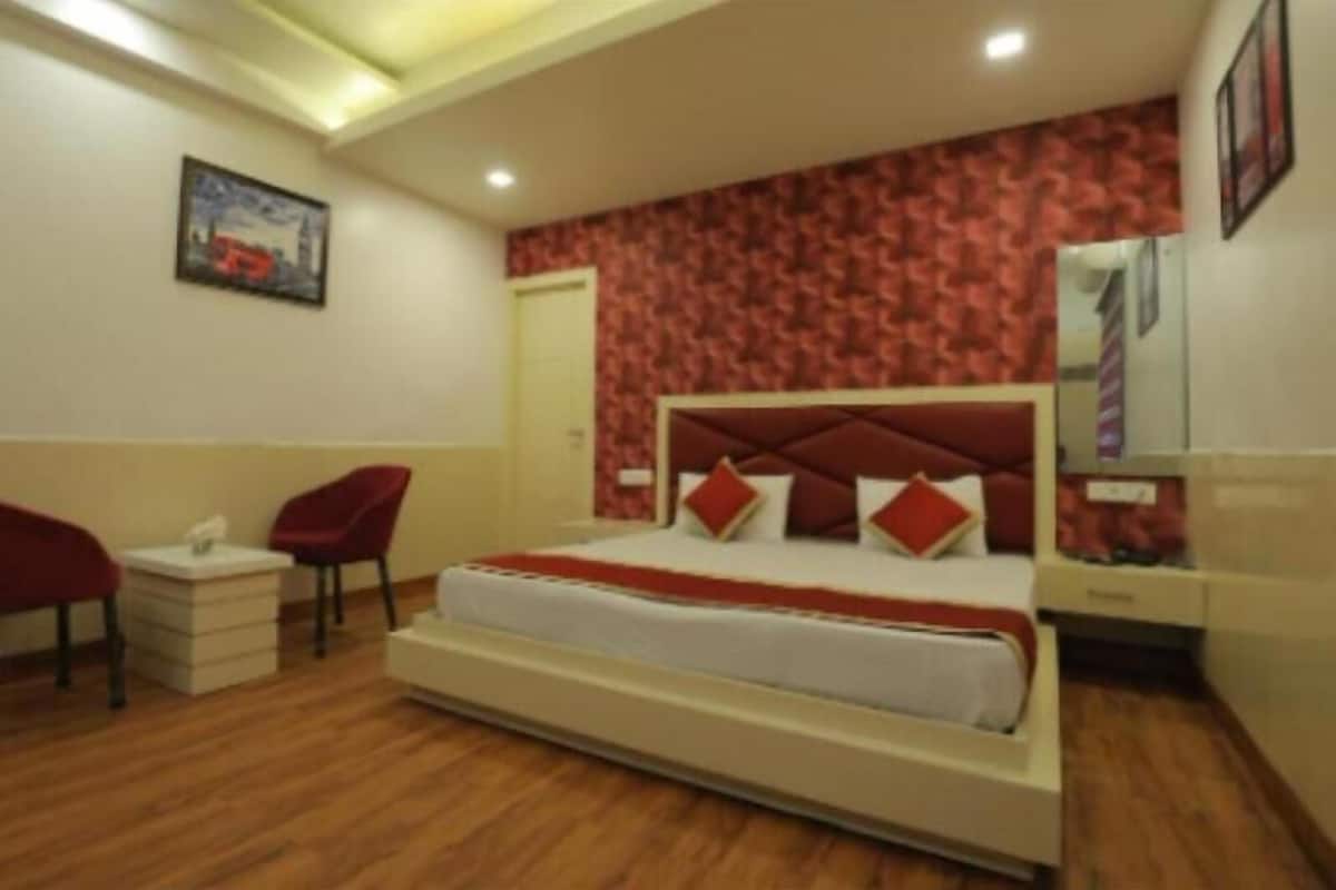 Une chambre d’hôtel avec un grand lit, deux fauteuils rouges, une table de chevet et un mur décoré d’un motif rouge.