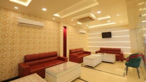 A modern hotel room with a patterned wallpaper, red sofas, a white coffee table, and a flat-screen TV mounted on the wall. - Hotel Sahibs Red Carpet (Agra)