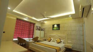 A modern hotel room with a large bed, bedside tables, a desk, and a ceiling fan. - Hotel Sahibs Red Carpet (Agra)